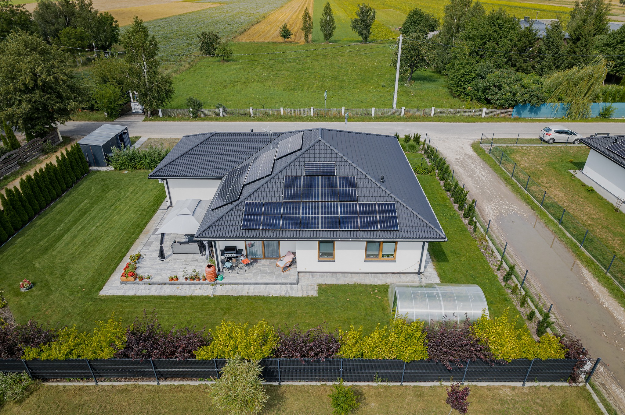 Widok z góry na nowoczesny dom jednorodzinny z panelami słonecznymi na dachu, tarasem i ogrodem w Białej Podlaskiej. Na tarasie widoczne meble ogrodowe i rośliny w donicach.
