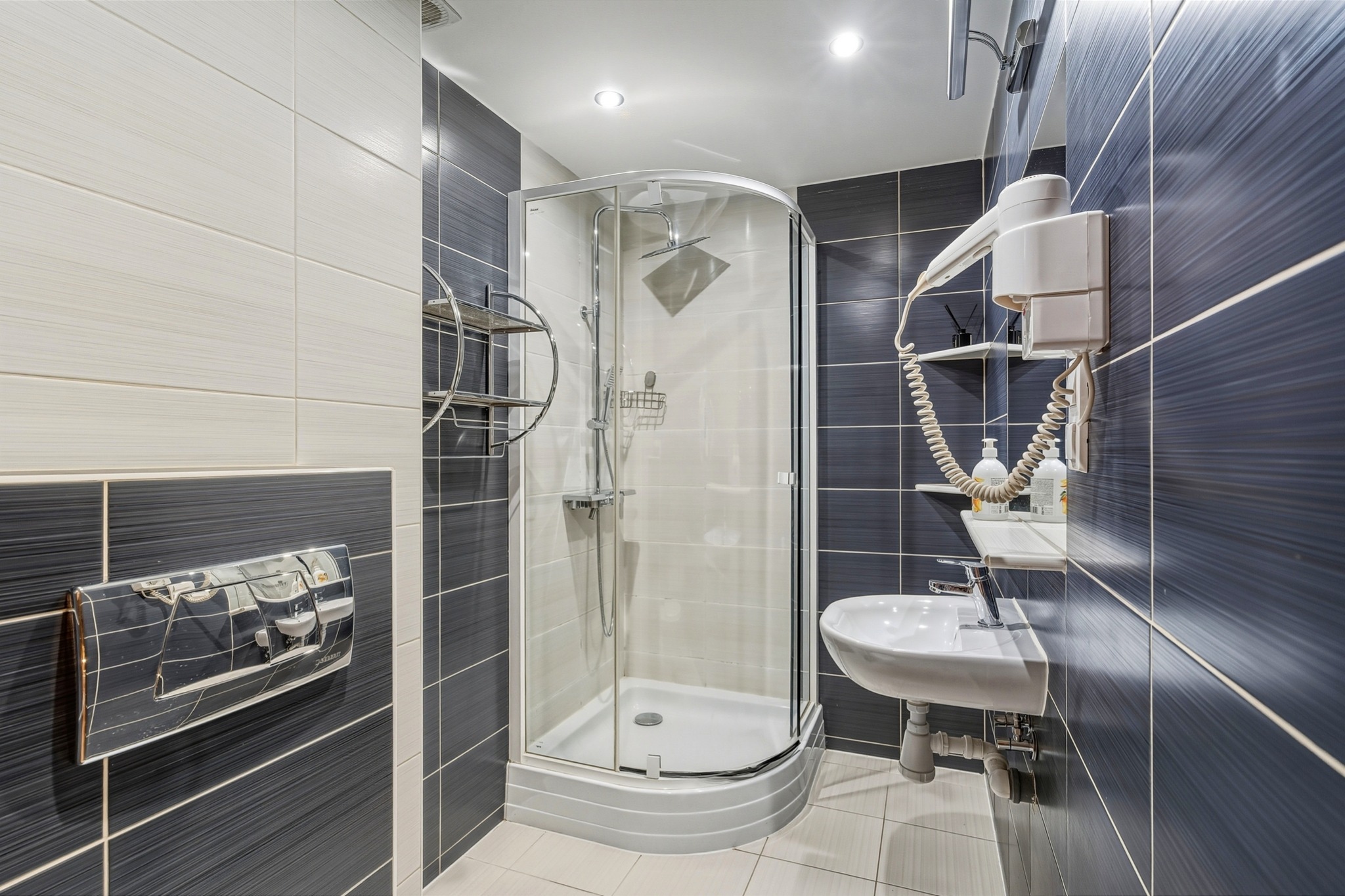 Nowoczesna łazienka z kabiną prysznicową, umywalką i grzejnikiem drabinkowym. Ciemne i jasne płytki na ścianach. Widoczne detale wykończenia.