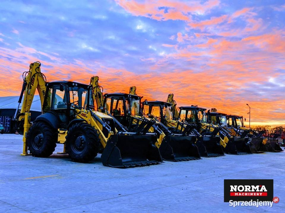 Rząd żółto-czarnych koparko-ładowarek New Holland ustawionych na placu, widoczny zachód słońca z pomarańczowymi chmurami w tle, logo firmy Norma Machinery w prawym dolnym rogu.