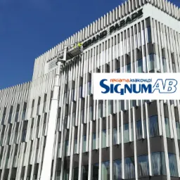 Montaż liter przestrzennych 'GRAND PARADE' na fasadzie budynku biurowego z użyciem podnośnika koszowego, widok z dołu na tle błękitnego nieba.