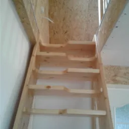 Drewniane schody strychowe z surowego drewna, prowadzące na poddasze wykończone płytami OSB, widoczne przewody elektryczne.