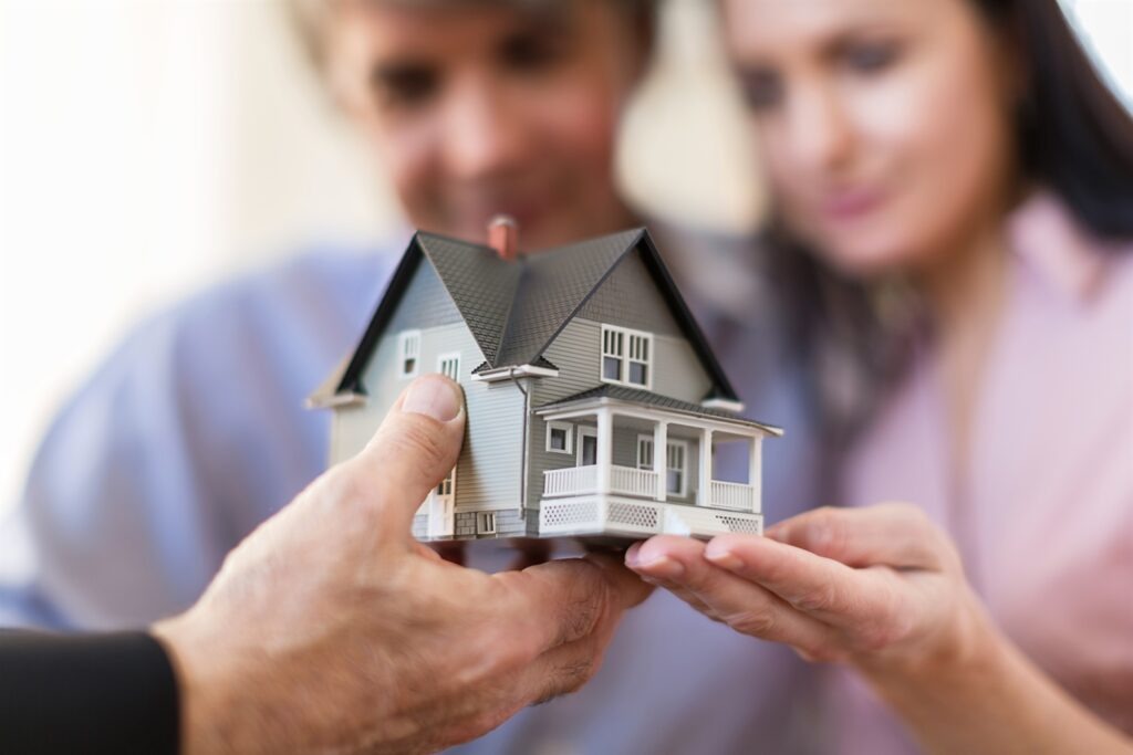 Model domu w dłoniach pary, potencjalna inwestycja mieszkaniowa.