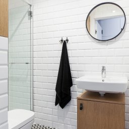 StudioRR MONIKA ROGOZIK-ROMANOWSKA - Nowoczesna łazienka z białą armaturą, ścianami wyłożonymi białymi, prostokątnymi płytkami w stylu metro i czarno-białą podłogą w geometryczne wzory. Na ścianie okrągłe lustro z czarną ramą i czarny...