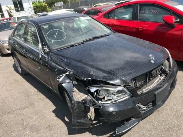 Czarny Mercedes z uszkodzonym przodem po kolizji, widoczne ślady po markerze na karoserii, w tle inne pojazdy na parkingu.