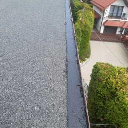 KMMJ Firma dekarska w Bielsku-Białej - Widok z góry na płaski dach pokryty papą, z widocznymi obróbkami blacharskimi i uszczelnieniami, w tle zabudowa jednorodzinna i zieleń.