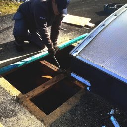 KMMJ Firma dekarska w Bielsku-Białej - Dekarz w trakcie naprawy dachu z użyciem łomu, widoczny otwór w poszyciu dachu i fragment świetlika dachowego