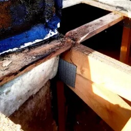 Odsłonięta konstrukcja dachu z widoczną warstwą izolacji i fragmentem starego pokrycia, po demontażu części dachu, z bliska.