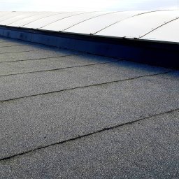 KMMJ Firma dekarska w Bielsku-Białej - Dach pokryty papą z widocznymi łączeniami i niewielkimi pęknięciami, z elementem doświetlającym w górnej części.