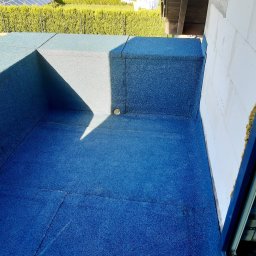 KMMJ Firma dekarska w Bielsku-Białej - Płaski dach pokryty niebieską papą termozgrzewalną, widoczny kominek wentylacyjny i fragment ściany budynku z ociepleniem.