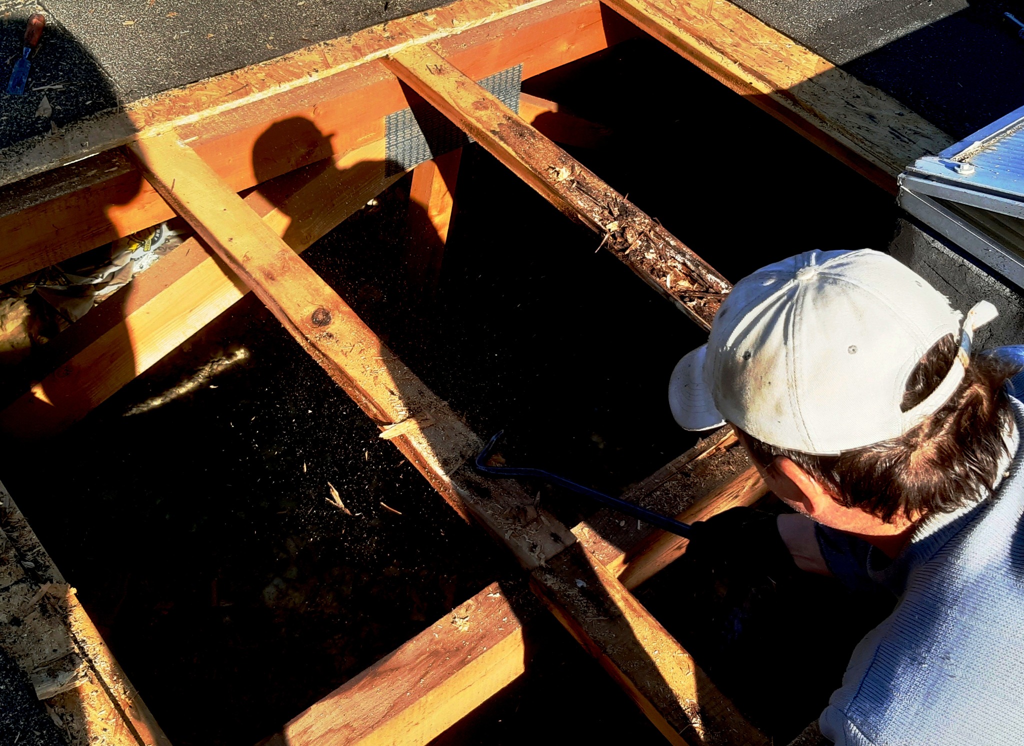 Pracownik w czapce demontuje drewnianą konstrukcję dachu przy użyciu łomu, widok z góry na częściowo odsłonięty dach.