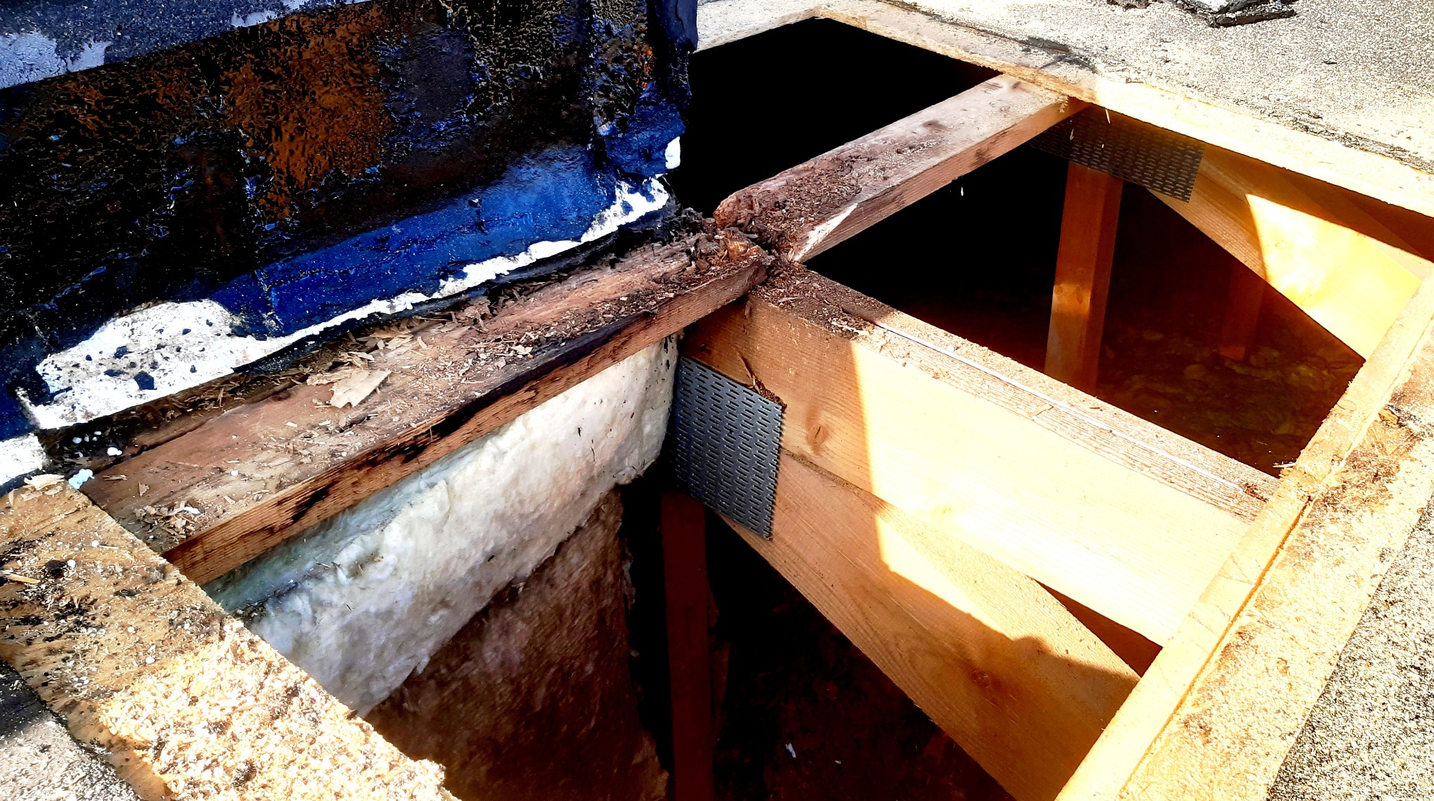 Odsłonięta konstrukcja dachu z widoczną warstwą izolacji i fragmentem starego pokrycia, po demontażu części dachu, z bliska.