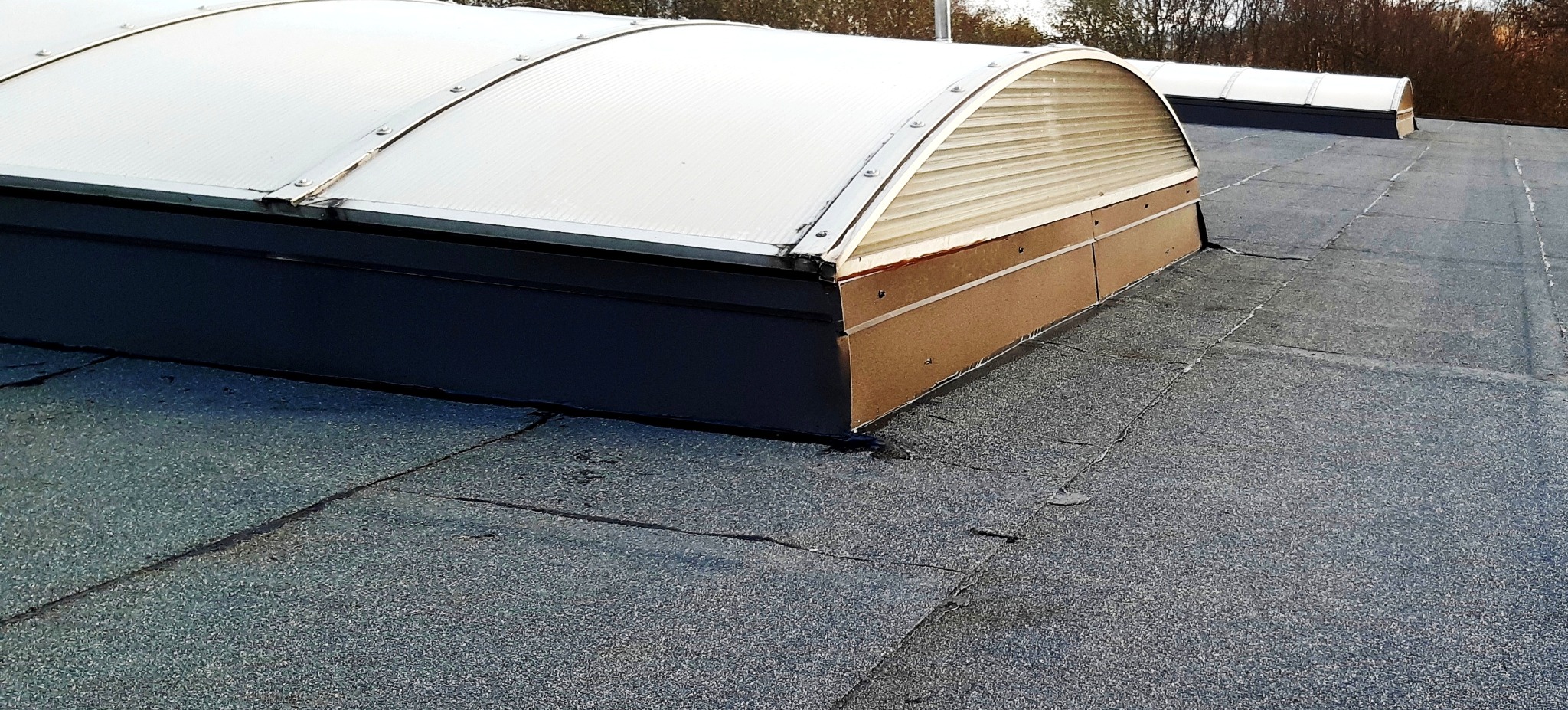 Widok z góry na płaski dach pokryty papą z zainstalowanymi świetlikami dachowymi o półokrągłym kształcie, widoczne detale łączeń i uszczelnień.