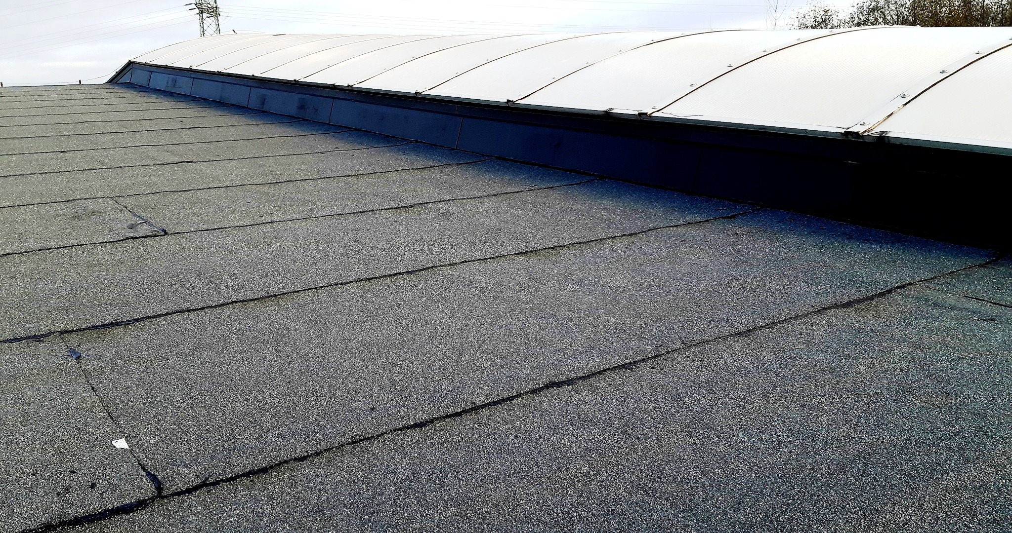 Dach pokryty papą z widocznymi łączeniami i niewielkimi pęknięciami, z elementem doświetlającym w górnej części.