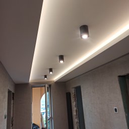 Delta - Wykończone wnętrze z podwieszonym sufitem z oświetleniem LED i punktowymi lampami, widoczne surowe ściany i otwarte przejścia drzwiowe.