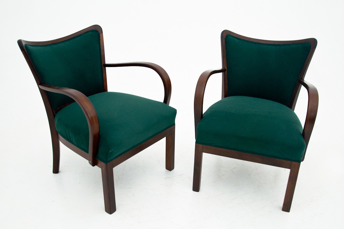 Dwa odnowione fotele w stylu art deco z ciemnozieloną tapicerką i giętymi drewnianymi podłokietnikami, ustawione na białym tle.