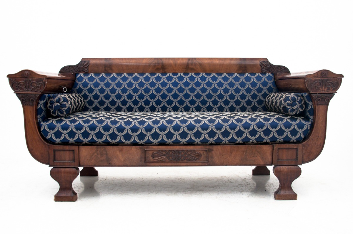 Antyczny drewniany kanapa z niebieską tapicerką w geometryczny wzór i zdobieniami snycerskimi na bokach i froncie, na białym tle.