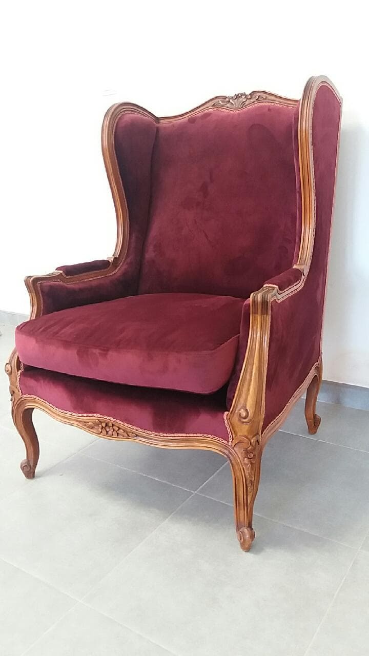 Burgundowy fotel uszak z drewnianą ramą o zdobnych nogach, stojący na jasnych płytkach.