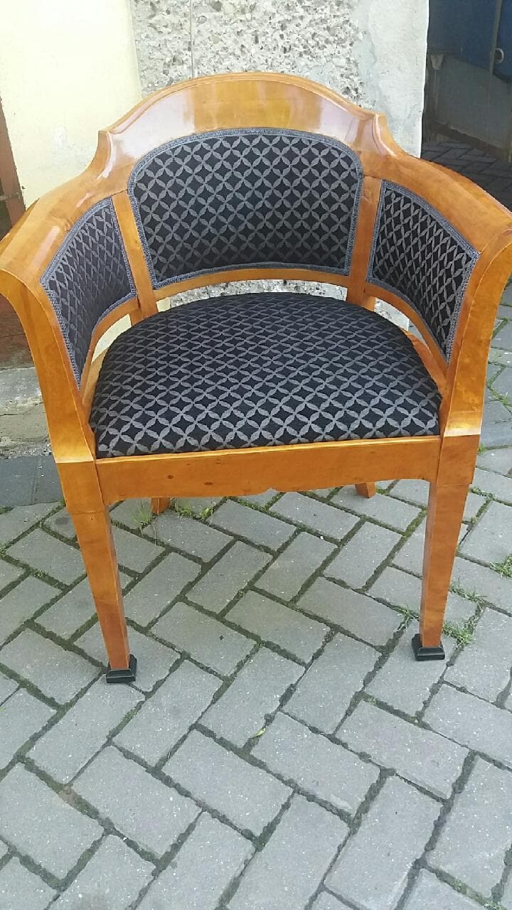 Odnowiony fotel z drewnianą ramą i tapicerką w geometryczny wzór, stojący na brukowanym podłożu.