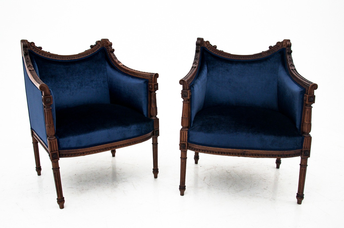 Para granatowych, aksamitnych foteli z ciemnego drewna, z rzeźbionymi detalami, stojących na białym tle.