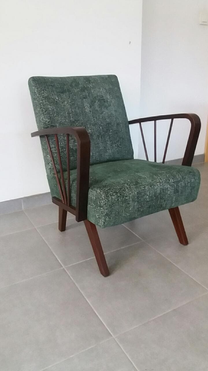 Odnowiony fotel w stylu vintage z zieloną tapicerką i ciemnobrązowymi drewnianymi elementami, stojący na szarych płytkach podłogowych.