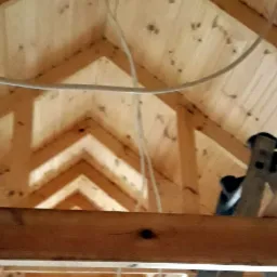 Drewniany szkielet poddasza z widocznymi belkami stropowymi, deskami i przewodami elektrycznymi w trakcie budowy.