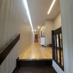 Korytarz z panelami podłogowymi, oświetleniem LED w suficie, schodami z drewnianą balustradą i odkurzaczem w tle.