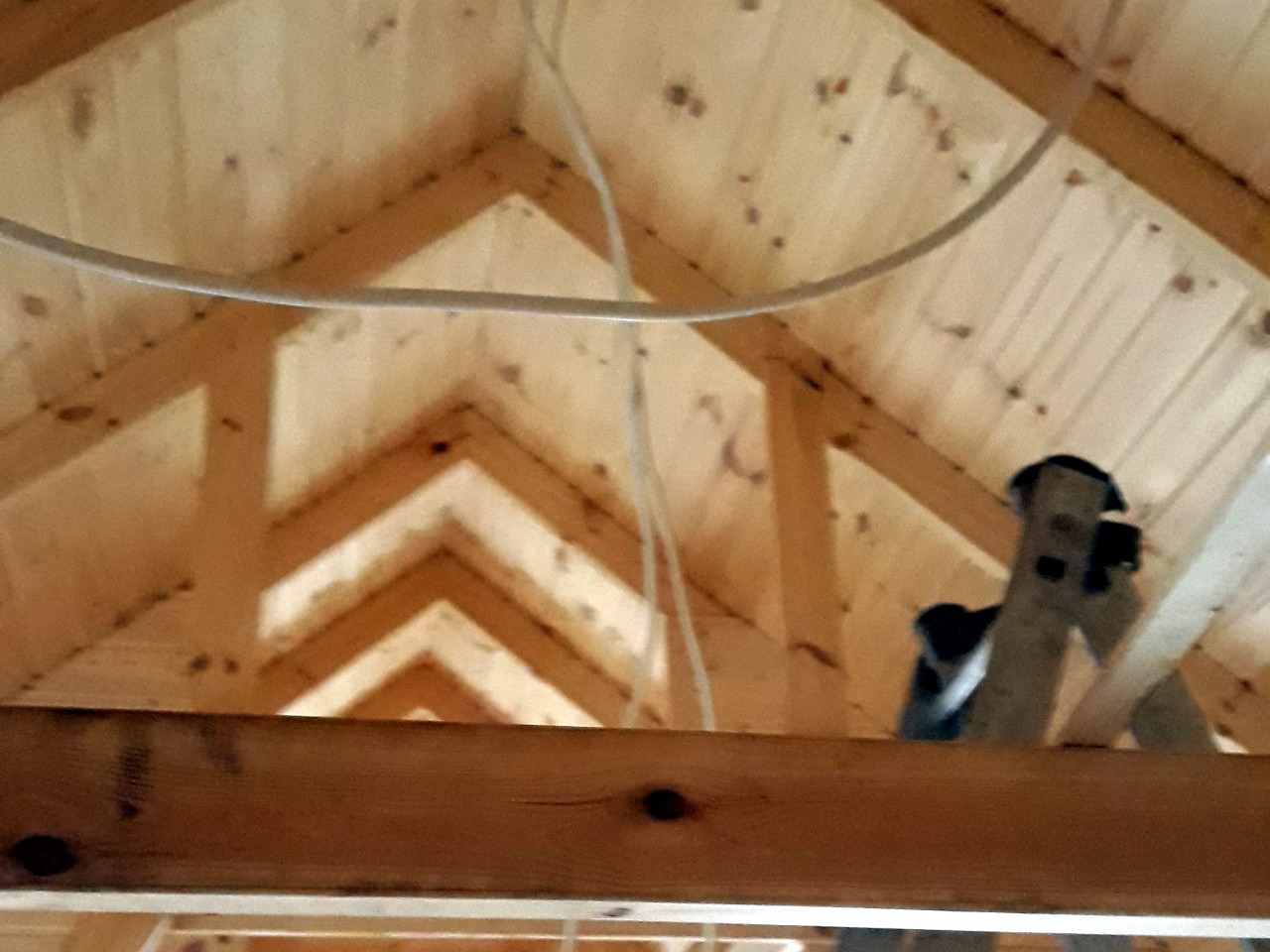 Drewniany szkielet poddasza z widocznymi belkami stropowymi, deskami i przewodami elektrycznymi w trakcie budowy.