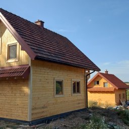 WRÓBELEK SPÓŁKA ZOO Piotr Wróbel - Nowo wybudowany, drewniany dom z czerwonym dachem, widok z boku, obok drugi dom w podobnym stylu oraz fragment murowanej konstrukcji.