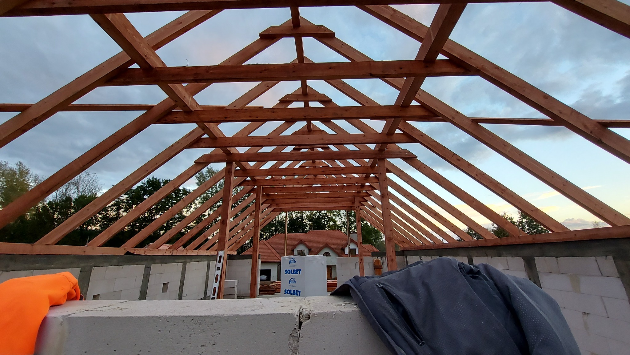 Konstrukcja drewniana dachu w trakcie budowy, widok od wewnątrz, z widocznymi belkami, bloczkami betonowymi i elementami izolacji Solbet w tle.