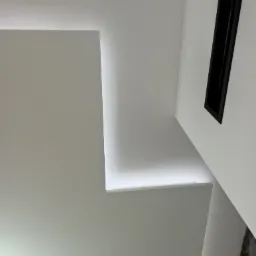 Nowoczesny, biały sufit z ukrytym oświetleniem LED, tworzącym geometryczne kształty, oraz czarny element dekoracyjny w ścianie.