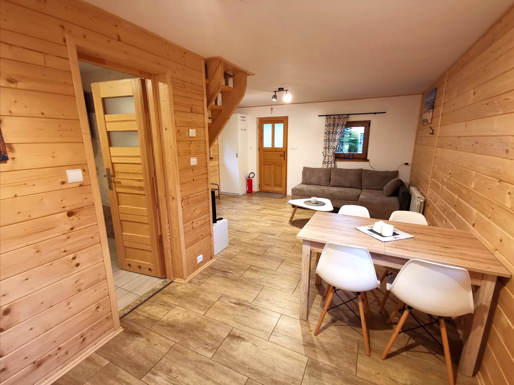 Drewniane wnętrze domu z widocznymi schodami, stołem z białymi krzesłami, kanapą i drzwiami wewnętrznymi