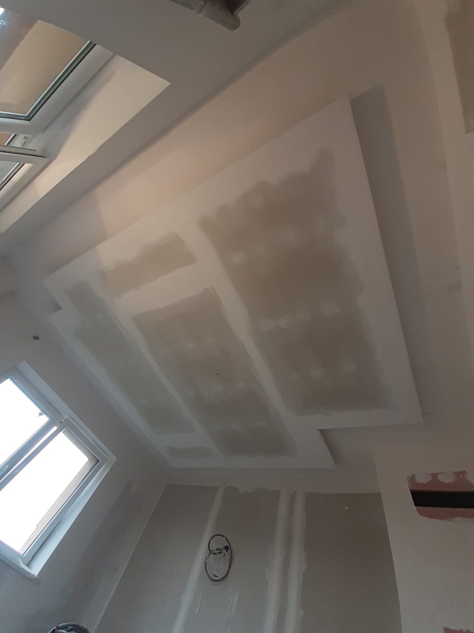 Sufit z płyt gipsowo-kartonowych w trakcie szpachlowania, widoczne okno dachowe oraz ślady po instalacji elektrycznej w ścianie.