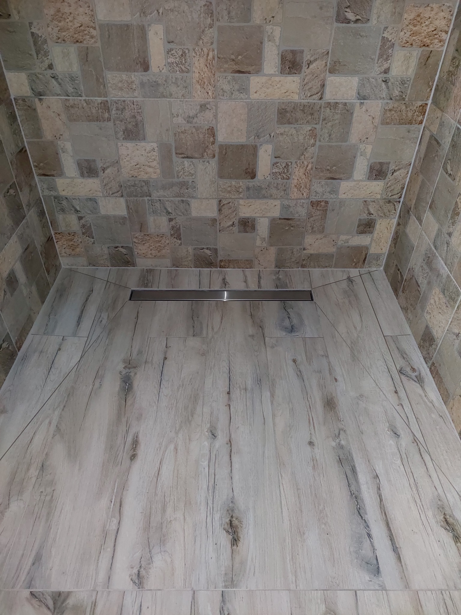 Wykończony brodzik kabiny prysznicowej z odpływem liniowym, wyłożony płytkami imitującymi drewno, ściany i sufit wyłożone mozaiką z kamienia naturalnego.