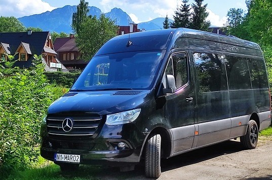 Czarny bus Mercedes-Benz Sprinter z panoramicznymi oknami, zaparkowany na tle górskiego krajobrazu z domami w Zakopanem.