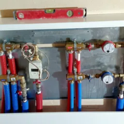 Instalacja wodna w szafce z widocznymi rurami w izolacji, licznikami wody i zaworami, poziomica na górze szafki.