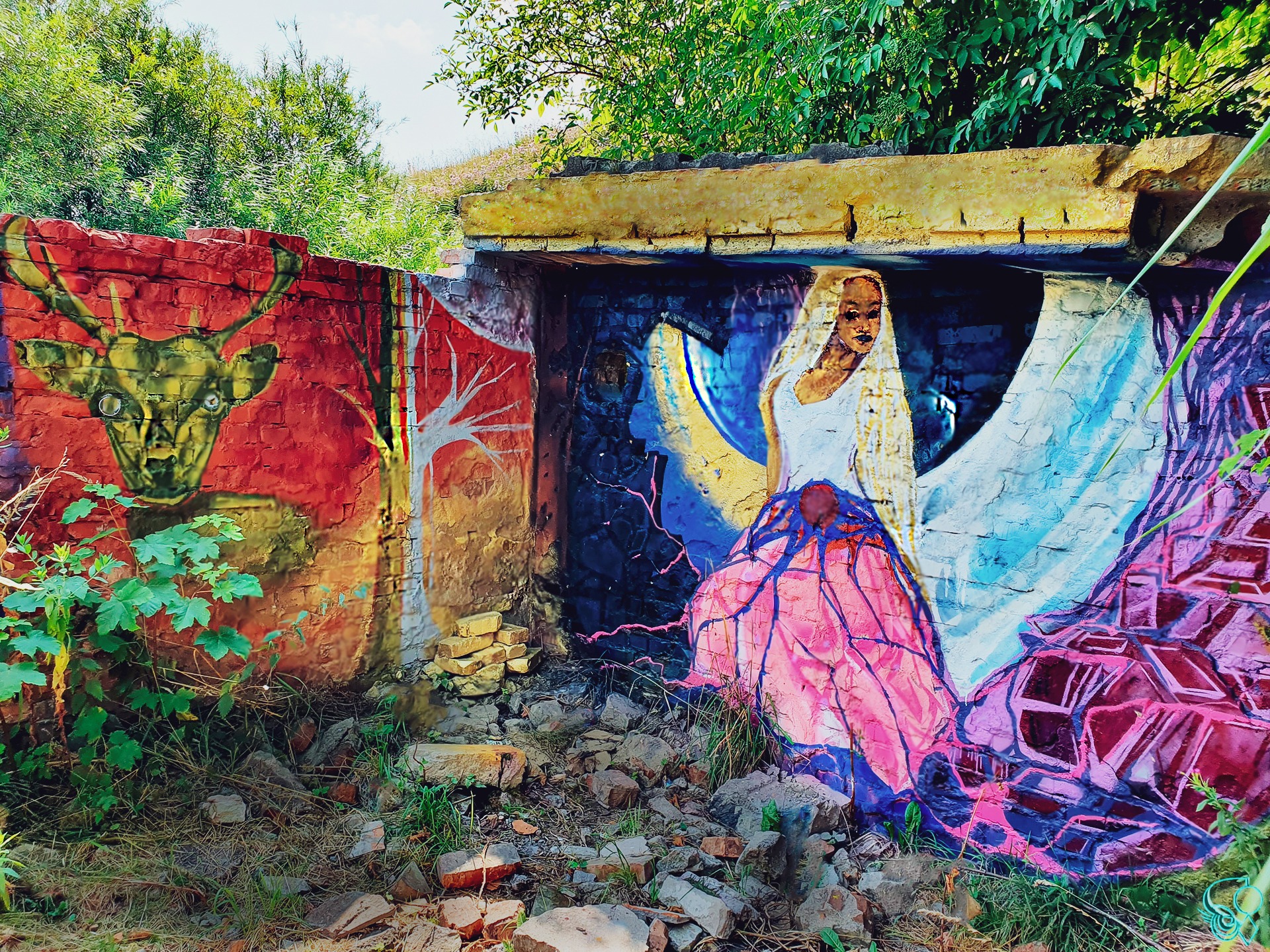 Kolorowe graffiti w Kołobrzegu przedstawiające jelenia i postać kobiecą na zrujnowanym murze z cegieł i betonu, otoczone zielenią i gruzem.