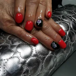 Dłoń z czerwonymi paznokciami, dwa paznokcie czarne z motywem białego kwiatka, na srebrnym pikowanym podłożu.