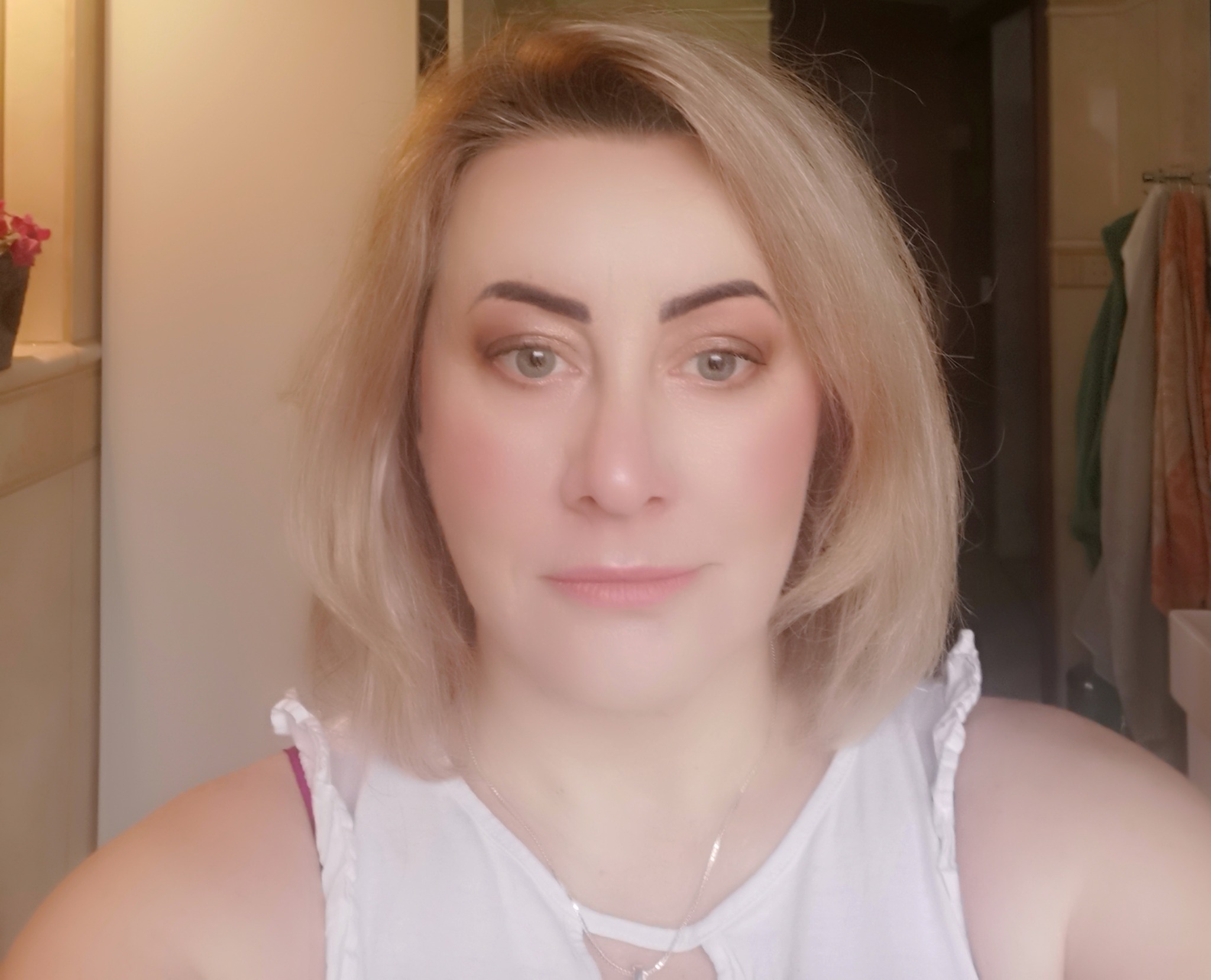 Portret kobiety z delikatnym makijażem oczu w odcieniach brązu i różu, blond włosy do ramion, srebrny naszyjnik, naturalne światło.