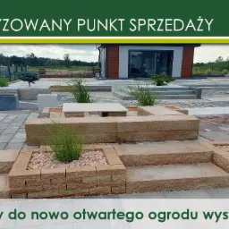 Ogród wystawowy z kostki betonowej i płyt drogowych, prezentujący różne aranżacje nawierzchni i elementy małej architektury, z widocznym budynkiem w tle.