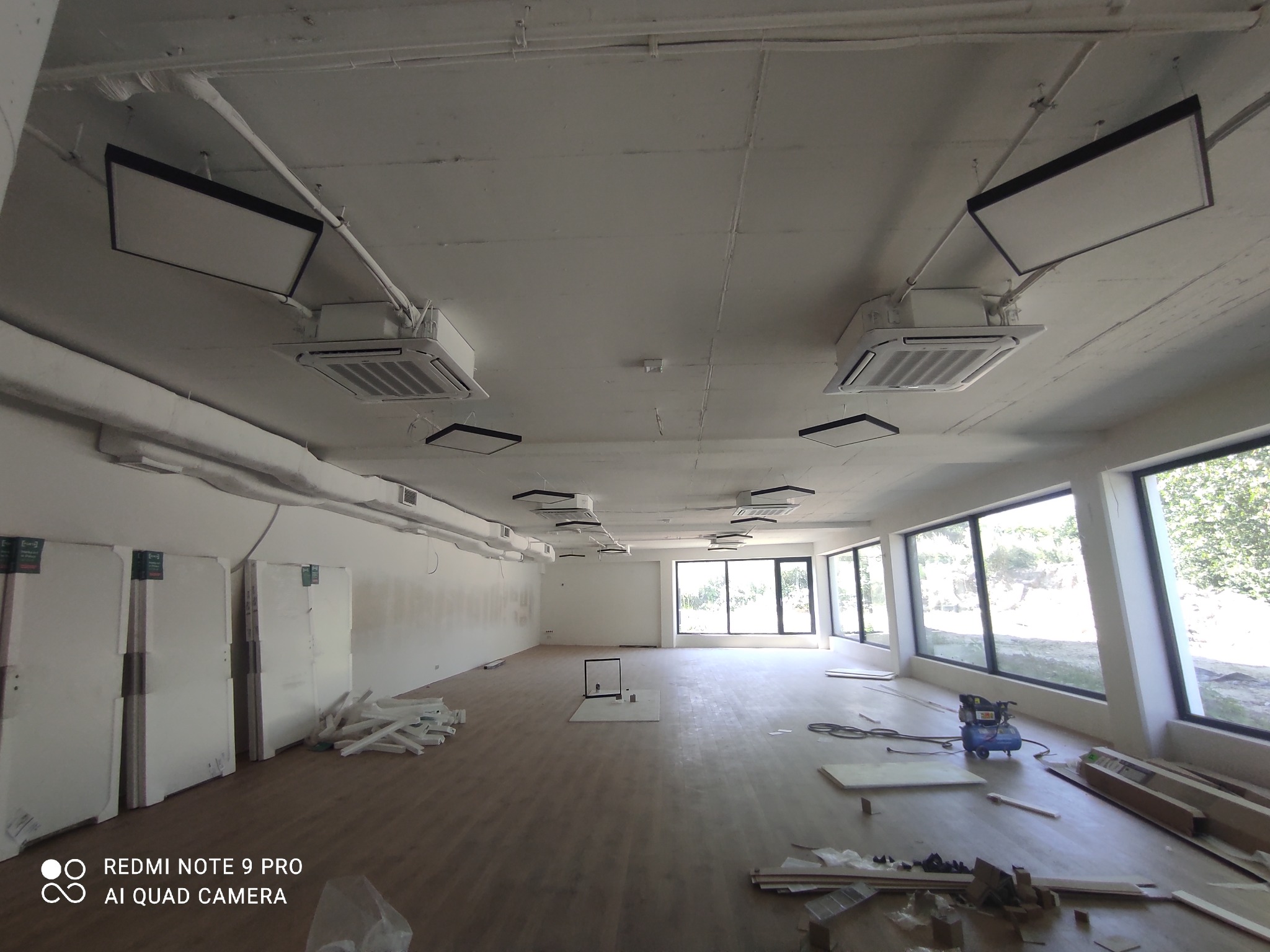 Montaż klimatyzacji kasetonowej w nowym lokalu, widoczne jednostki wewnętrzne i oświetlenie LED na suficie, kompresor na podłodze, przygotowane płyty gipsowe i inne materiały budowlane.