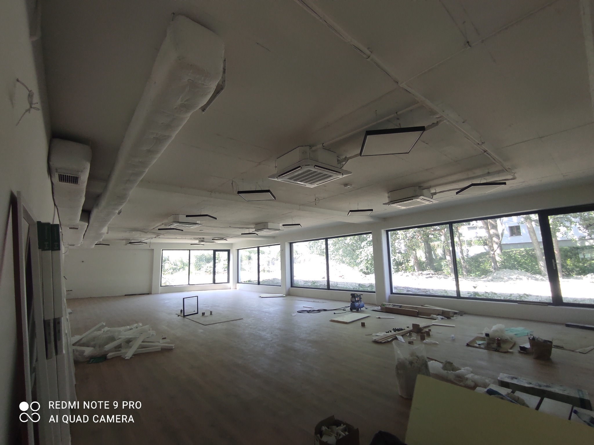 Wnętrze dużego pomieszczenia w trakcie instalacji klimatyzacji i wentylacji, widoczne kanały wentylacyjne pod sufitem, jednostki klimatyzacyjne i materiały budowlane na podłodze.