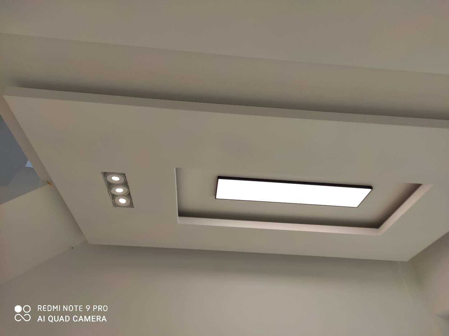 Podwieszany sufit z oświetleniem LED: trzy punktowe lampy i prostokątny panel, całość w odcieniach bieli.