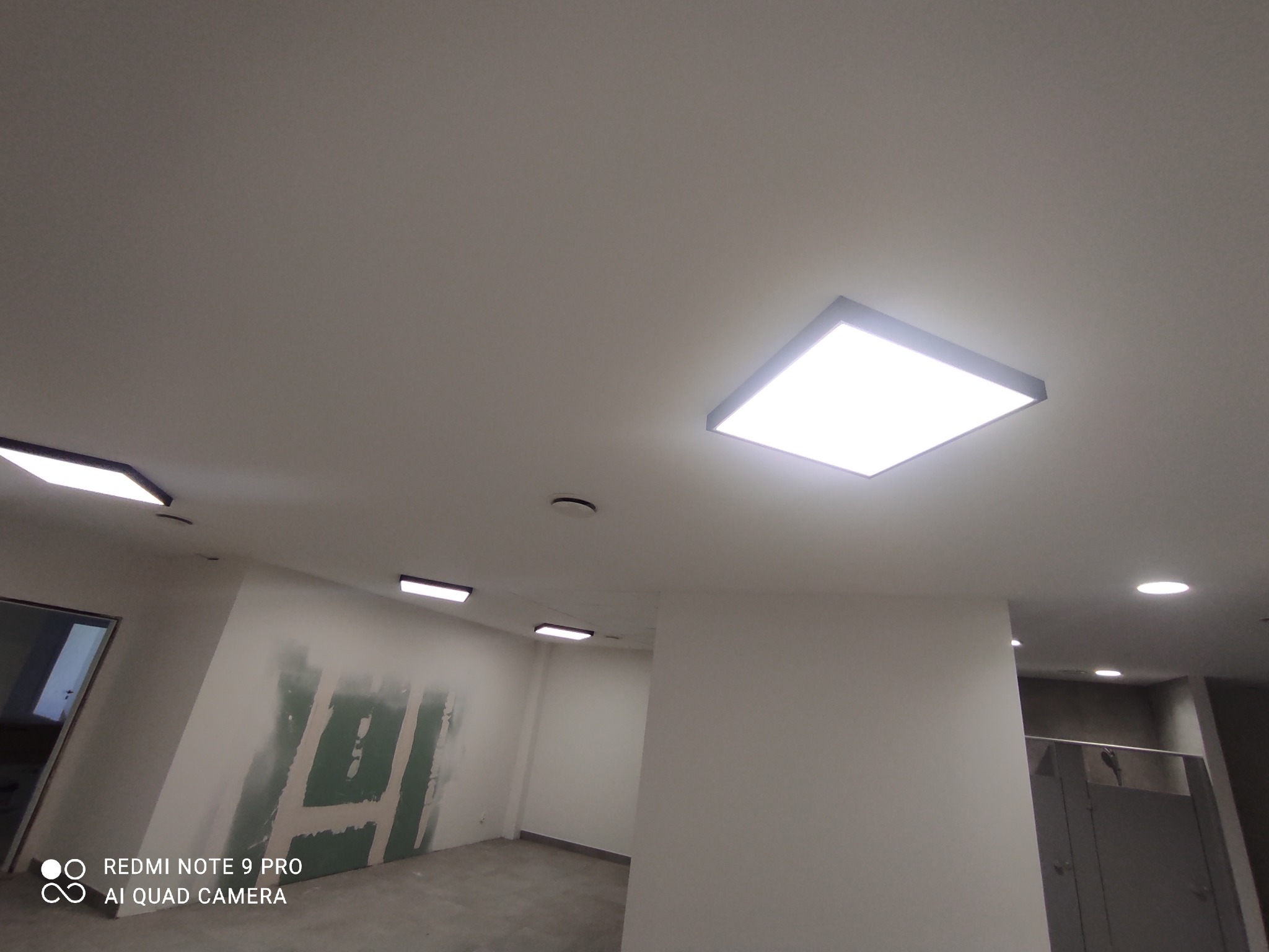 Kwadratowe panele LED w suficie podwieszanym w trakcie montażu, widoczne ślady po szpachlowaniu na ścianach.