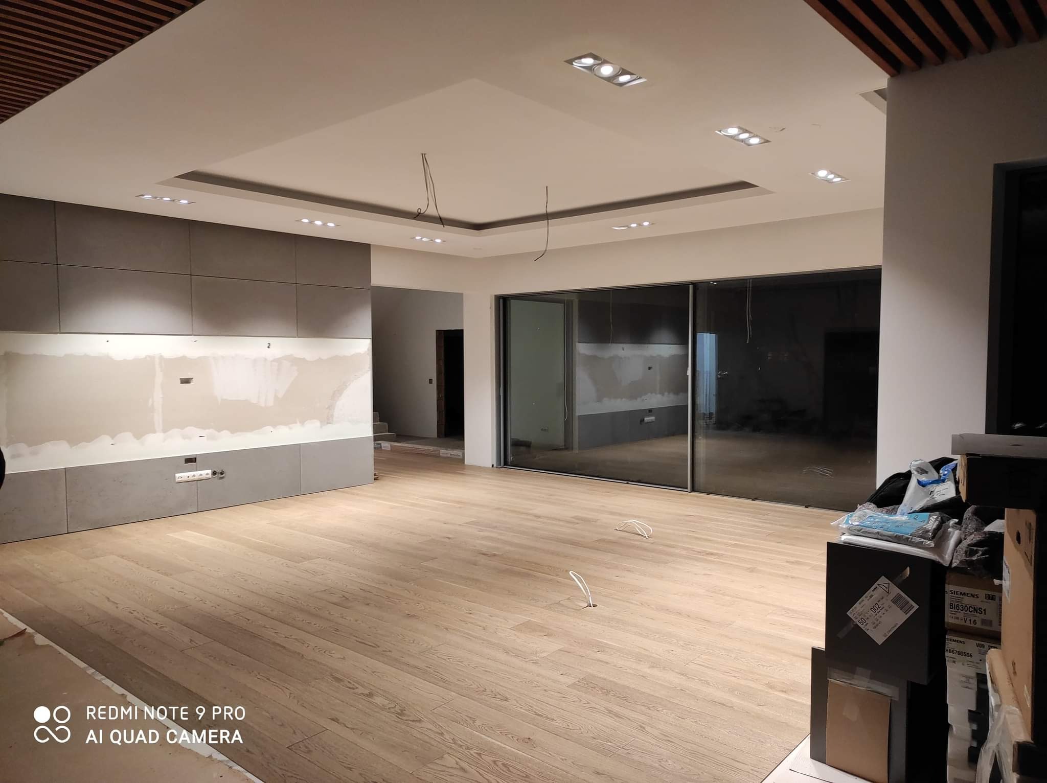 Wnętrze w trakcie prac wykończeniowych: widoczne podłączenia elektryczne wystające z podłogi, zabudowa ściany z gniazdkami oraz oświetlenie sufitowe w nowoczesnym stylu.