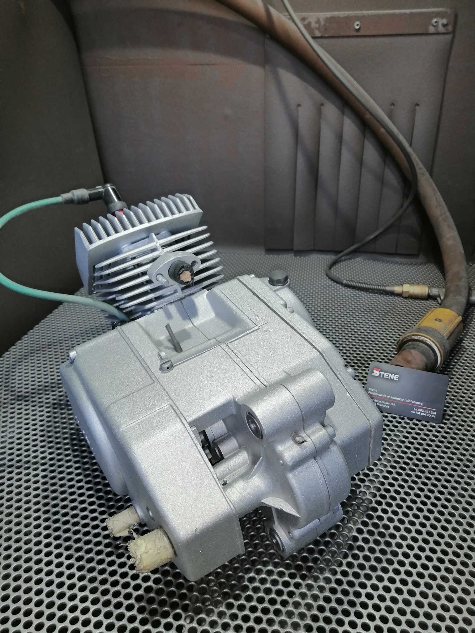 Silnik motocyklowy po piaskowaniu i malowaniu proszkowym na metalowej kratownicy, widoczna karta firmy STENE z adresem i numerem telefonu.