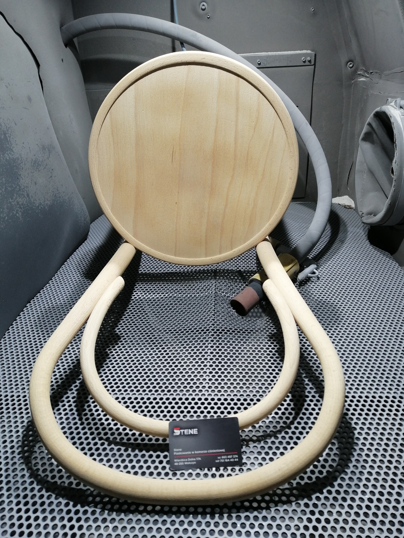 Drewniane elementy krzesła Thonet, przed obróbką, umieszczone wewnątrz komory do piaskowania. Widoczny dysk siedziska i gięte elementy oparcia oraz wizytówka firmy.