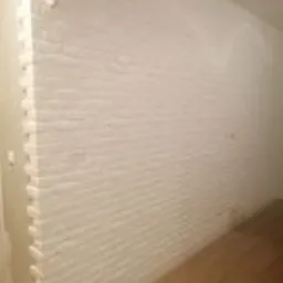 Ściana wykończona białymi panelami imitującymi cegłę, widok z bliska, widoczna podłoga z paneli.