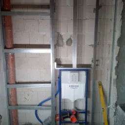 Stelaż podtynkowy Grohe zamontowany w surowej łazience z widocznymi rurami kanalizacyjnymi i poziomnicą opartą o ścianę.