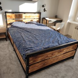 FilART - Construction Damian Filar - Drewniane łóżko z metalową ramą i pościelą w gwiazdy, widok z dołu, w tle biurko i okno z kwiatami.