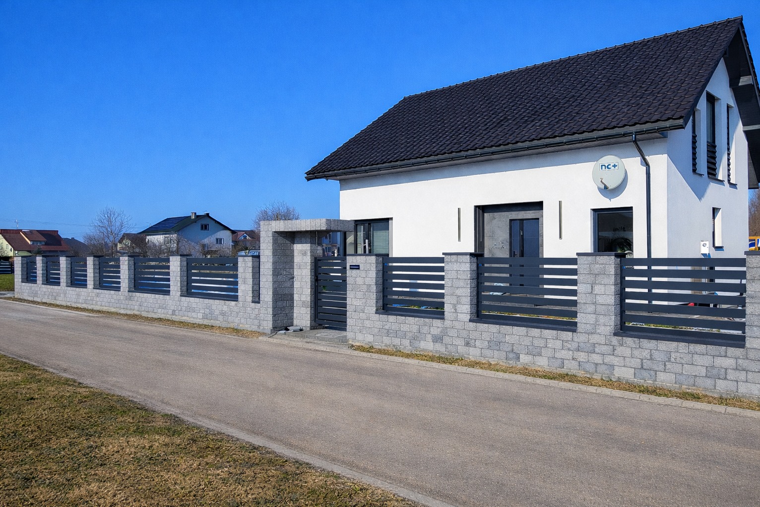 Nowoczesne ogrodzenie panelowe z szarej kostki i metalowych przęseł, brama wjazdowa, dom w tle, słoneczny dzień.